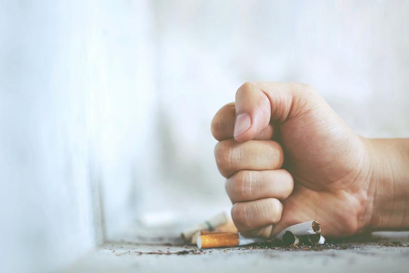 Iemand slaat met een vuist op een stapel opgebrande sigaretten.